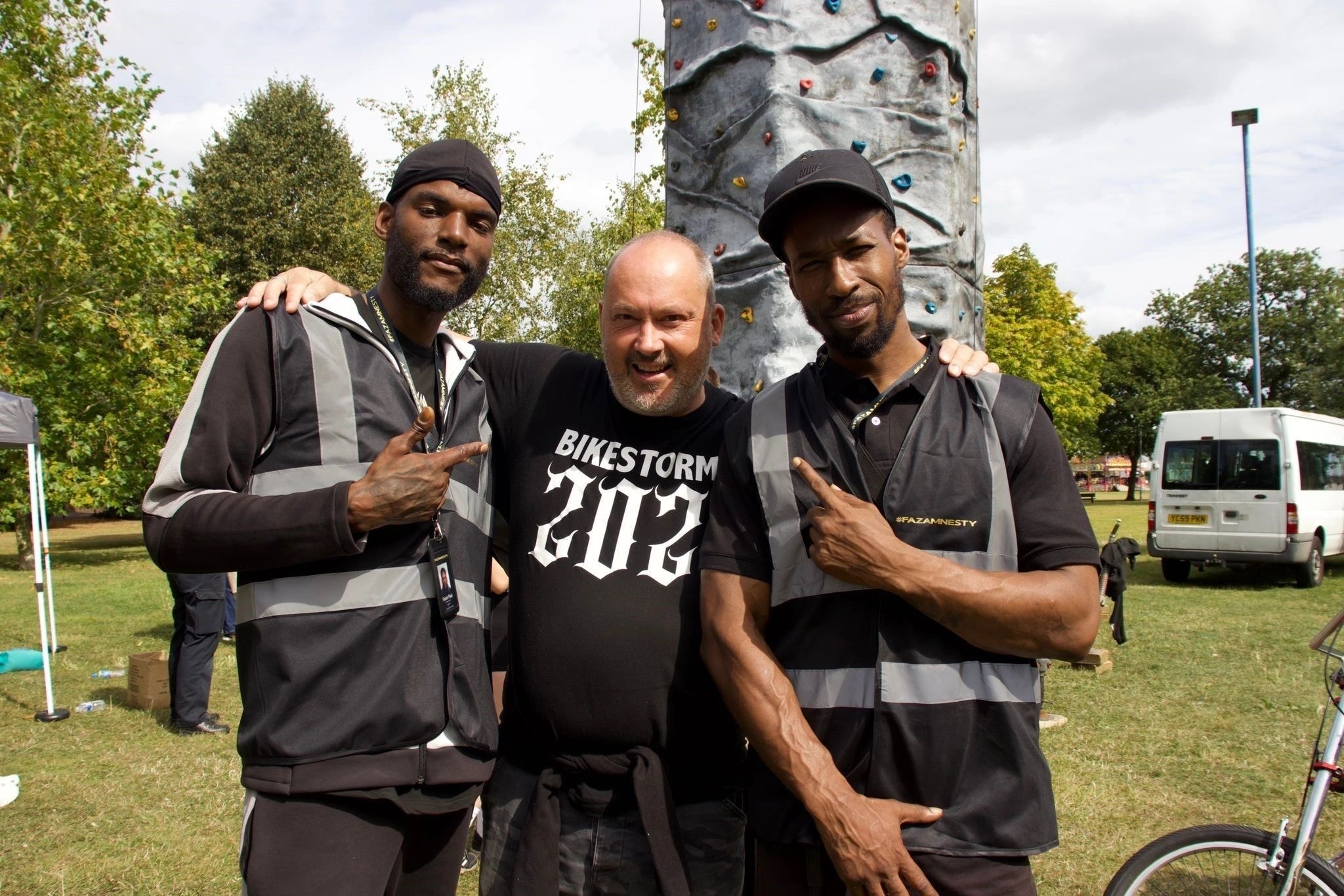 Three men posing by a climbing wall at a CAV community event